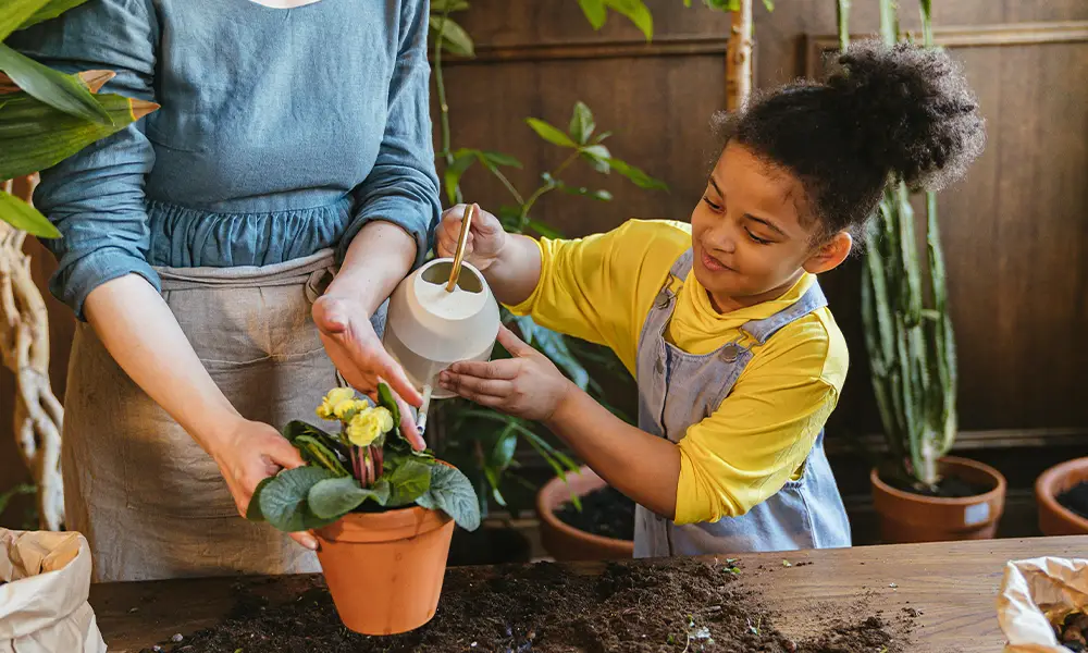 woman helping girl water plant
